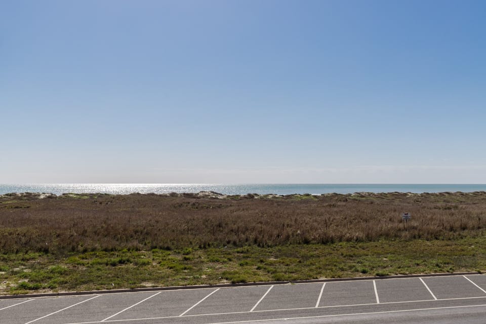 Coastal parking area with natural vegetation leading to ocean views under clear blue skies.