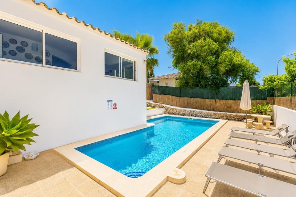 Modern white vacation villa featuring a private outdoor swimming pool, poolside sun loungers, and lush green landscaping.