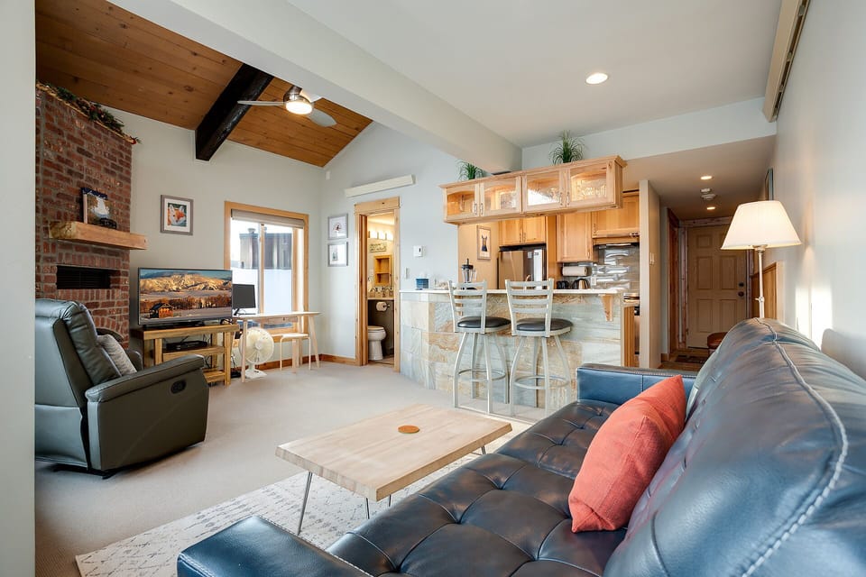 Your open-concept living space blends mountain charm with modern comfort—leather seating, rustic beams, and a cozy fireplace create the perfect après-ski retreat.
