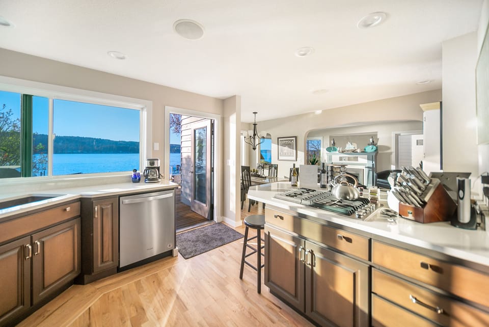 Bright kitchen with quartz counter tops, SS gas range, door leads out to deck. 