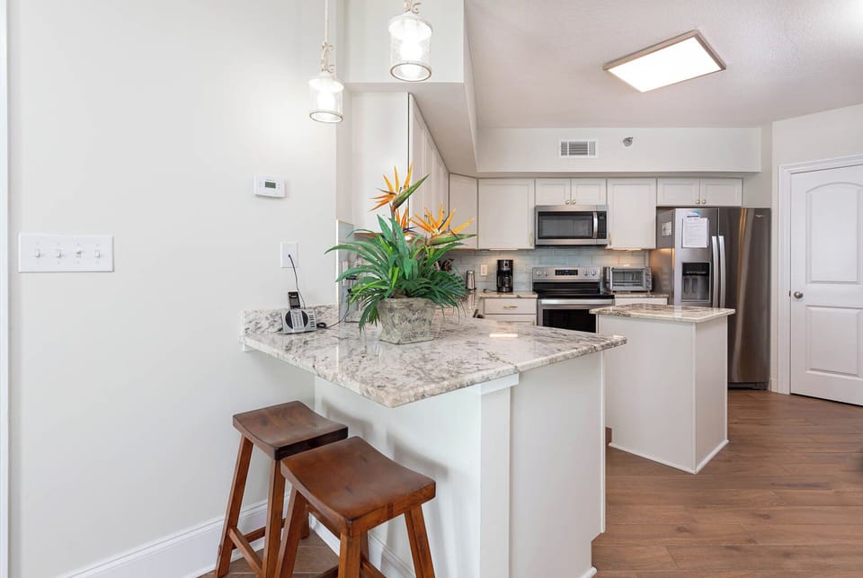 This modern kitchen features sleek stainless appliances, granite countertops, and a cozy breakfast bar with two wooden stools