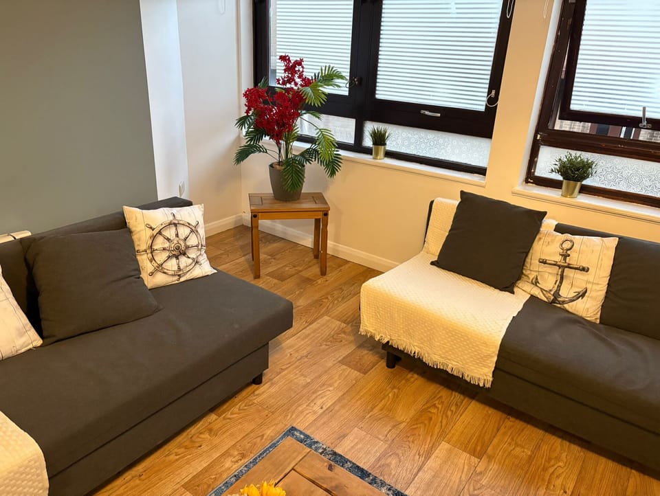 Bright living room with two grey sofas, coffee table, and floral centerpiece by large windows