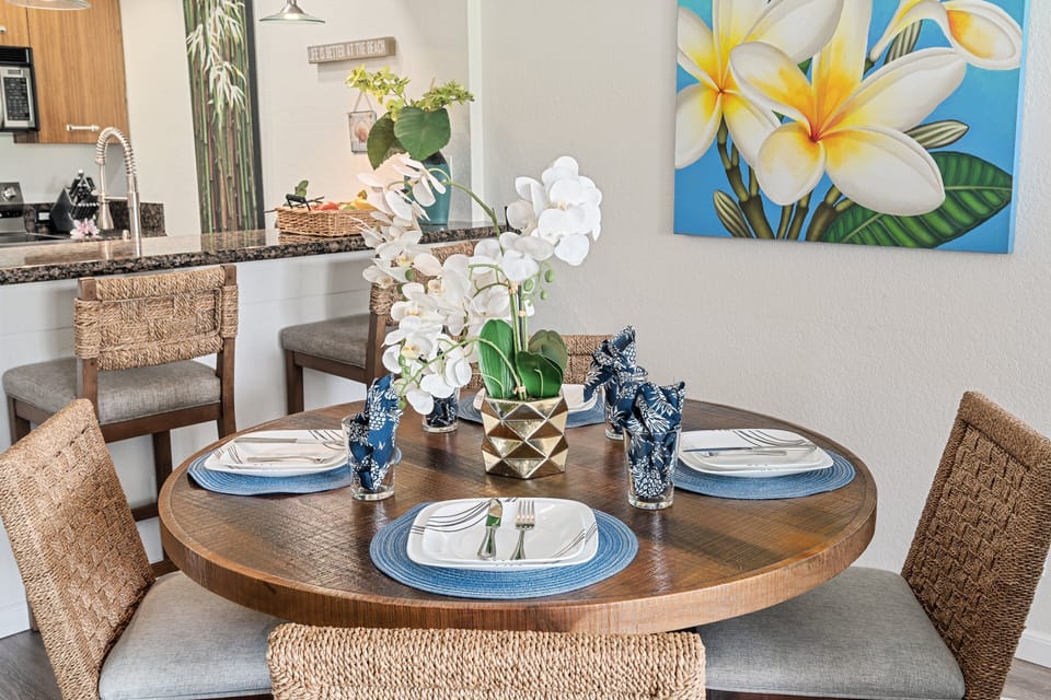 Table set with blue napkins and orchids, plumeria painting blooming softly on the wall.