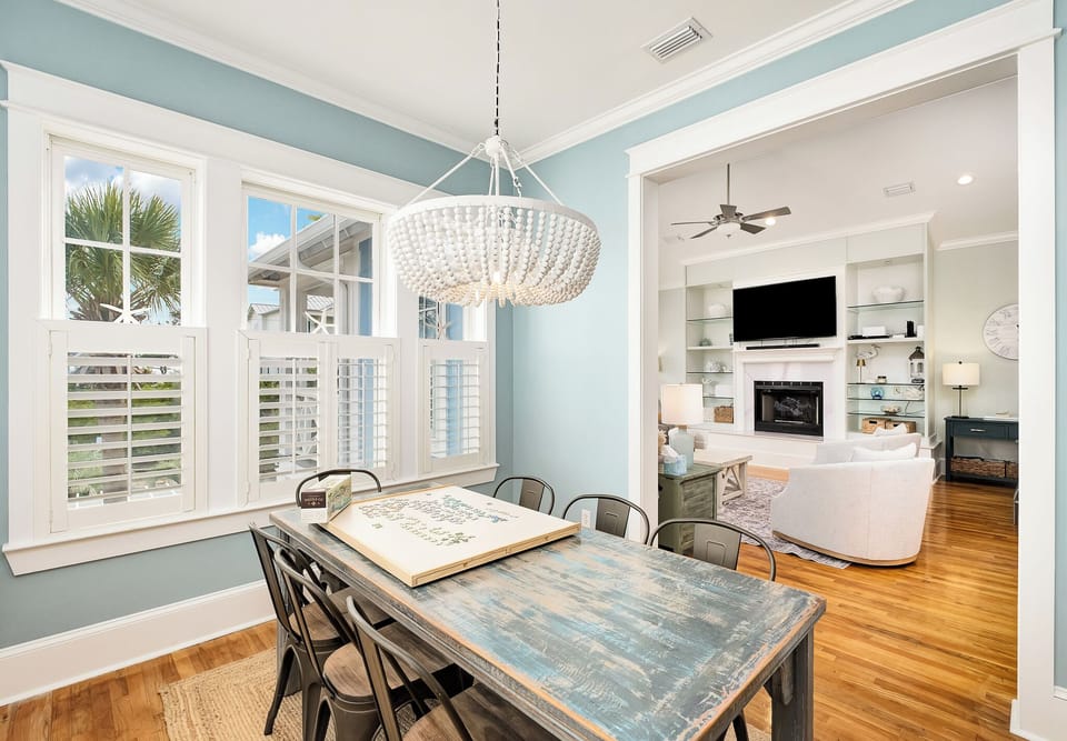 Your coastal dining room awaits with elegant chandelier lighting and rich hardwood floors flowing into the cozy living space beyond.