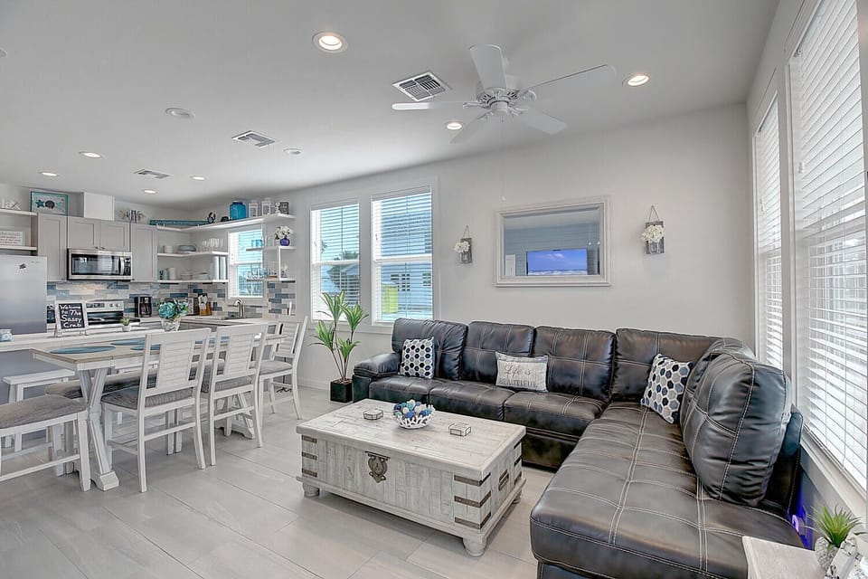 Relax in your open-concept living space featuring a plush leather sectional, fully equipped kitchen, and coastal decor that creates a perfect beach getaway.
