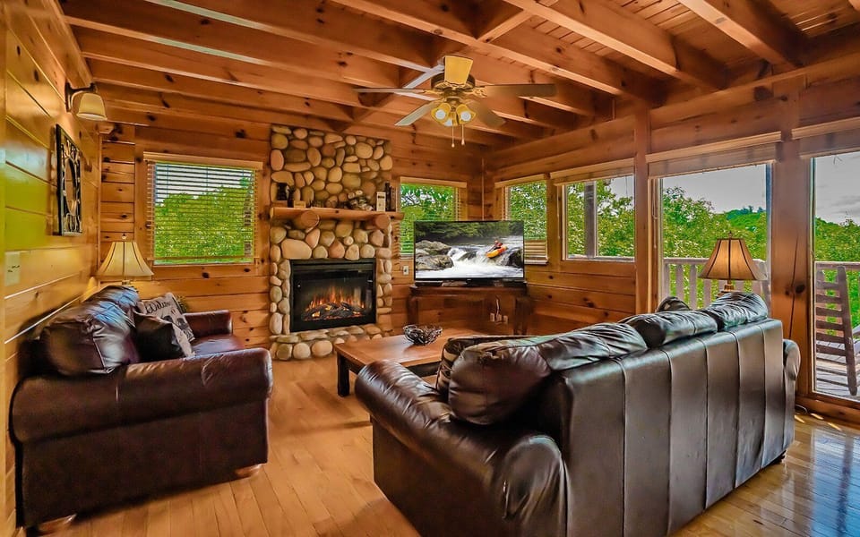 Cozy living room with leather seating, stone fireplace, and flatscreen TV.