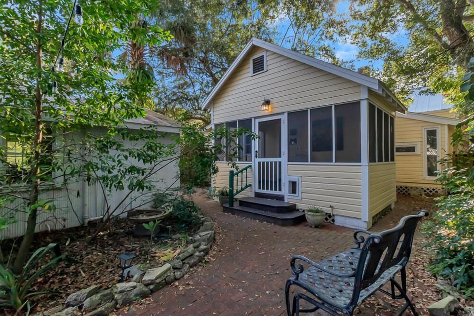 Adorable screened in rear patio tucked behind trees with a brick pathway entrance.