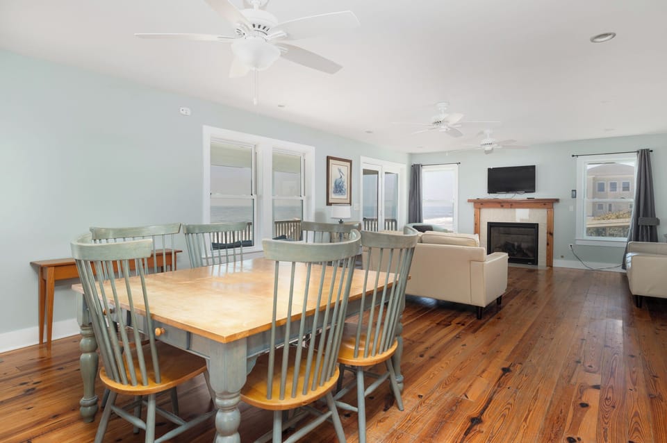 Relax in your spacious open-concept living space featuring warm hardwood floors, cozy fireplace, and stunning ocean views through floor-to-ceiling windows.