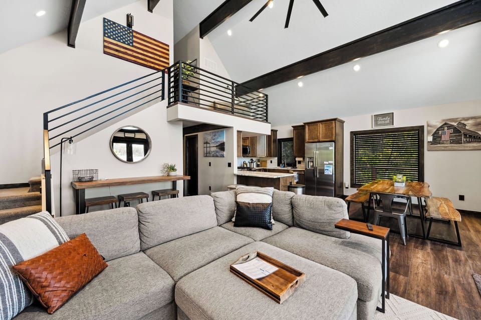 Relax in your open-concept living space with soaring ceilings, exposed beams, and a cozy sectional perfect for unwinding. The stylish loft, modern kitchen, and rustic-chic dining area create a welcoming retreat.