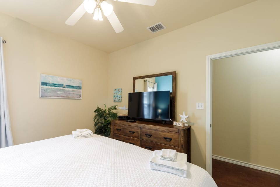 Relax in your peaceful bedroom with coastal artwork, flat-screen TV, and fresh towels waiting on your comfortable bed.