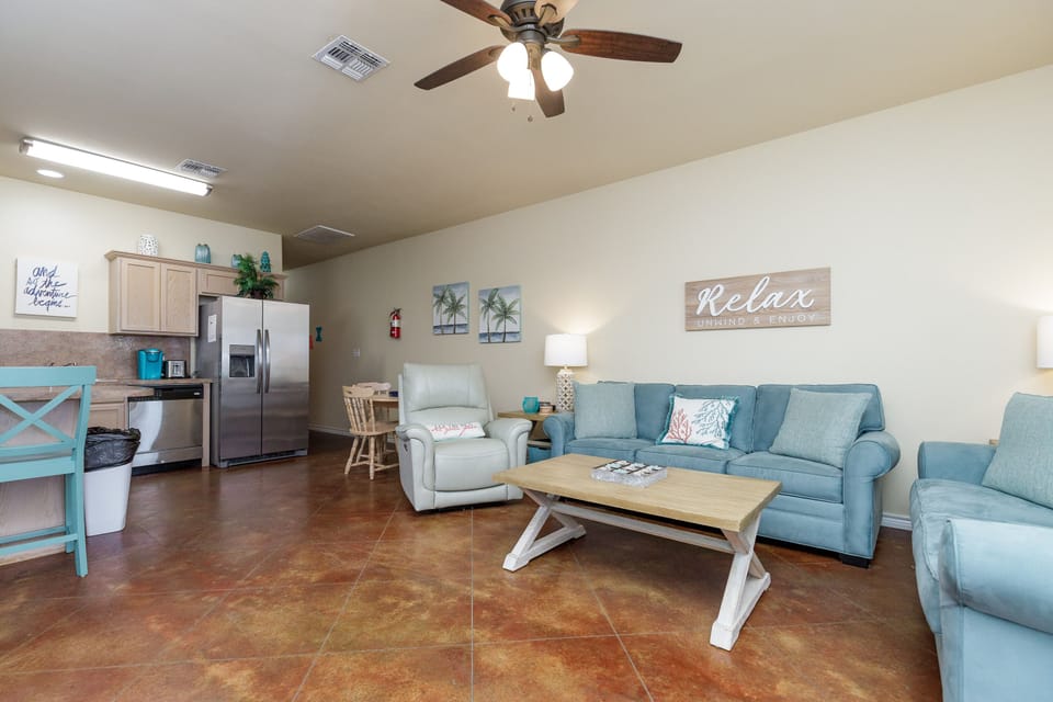 Unwind in your spacious living area with comfortable blue seating, modern kitchen, and coastal touches that invite you to truly relax.