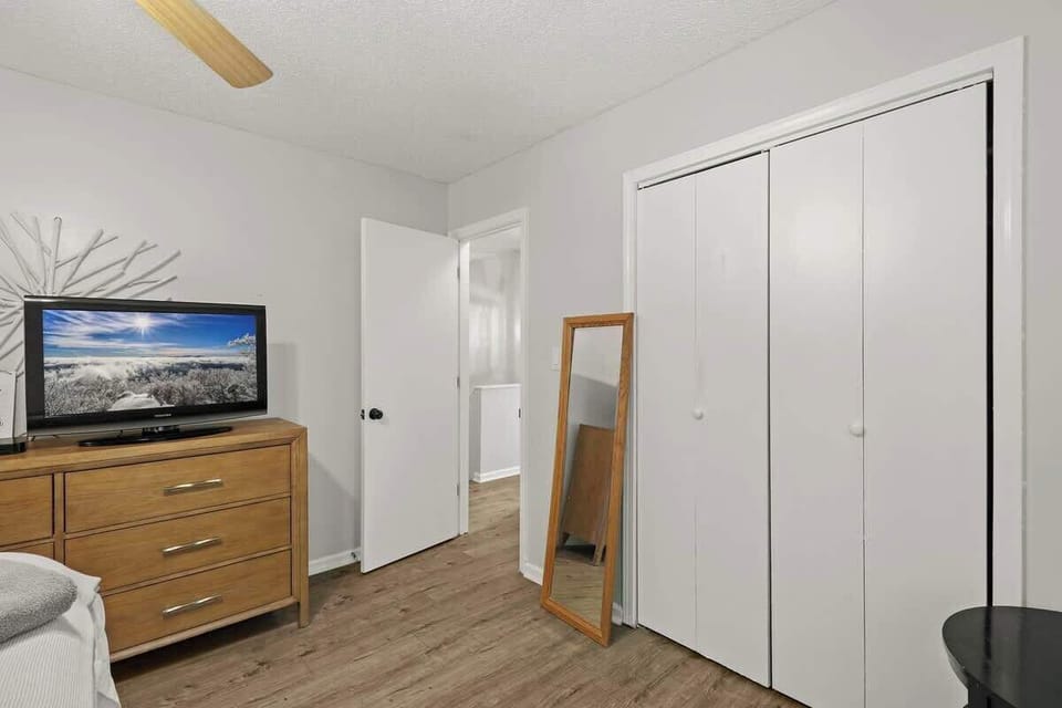 Elegant master suite: king-size bed, smart TV, indoor fireplace, walk-in closet, nightstands with reading lamps, and a stylish long mirror.