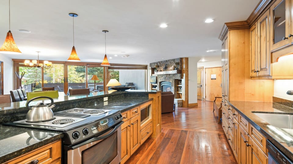 Step into your gourmet kitchen where rich wood cabinetry, gleaming granite counters, and a spacious island invite you to cook and gather. Natural light pours through expansive windows framing forest views.