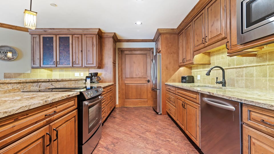 Picture yourself preparing meals in this spacious, fully equipped kitchen featuring rich wood cabinetry, granite countertops, and modern stainless steel appliances—perfect for your mountain getaway.