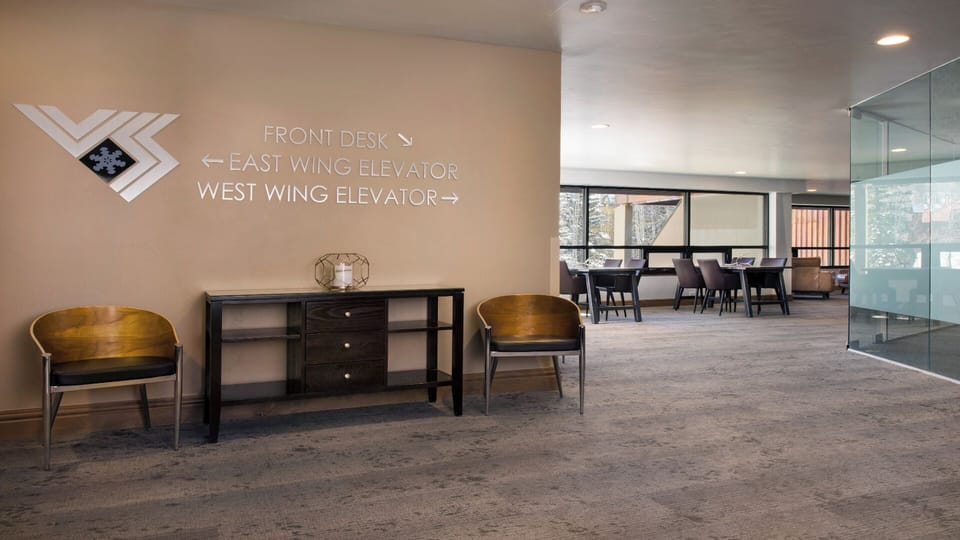 Welcoming lobby area with clear signage directing you to the front desk and elevators, featuring comfortable seating and modern, clean design throughout.