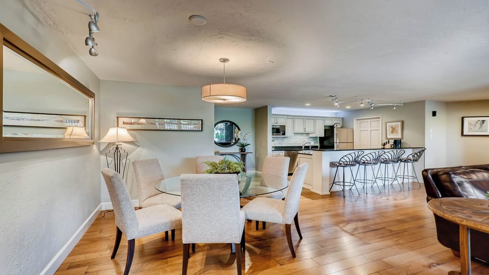 Picture yourself gathering around this glass dining table with family, then stepping into the bright open kitchen to prepare meals together—all under soft lighting and gleaming hardwood floors.