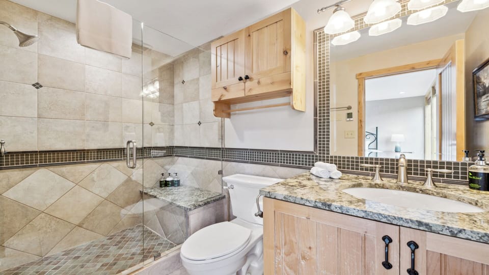 Step into your beautifully appointed bathroom featuring elegant tile work, a spacious walk-in shower, granite countertops, and warm wood cabinetry—everything you need to refresh and unwind.