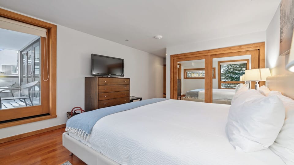 Sink into your plush bed with crisp linens and enjoy mountain views through elegant wood-framed windows. Your private balcony awaits morning coffee moments, while warm hardwood floors and stylish furnishings create a serene retreat.
