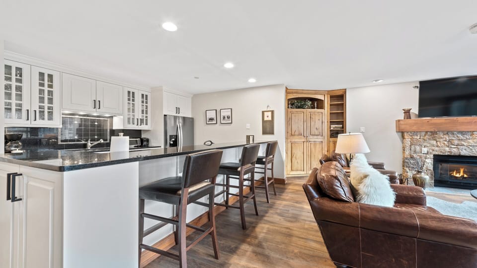 You'll love gathering in this open-concept living space where the sleek kitchen flows seamlessly into a cozy living area. Prepare meals at the granite-topped island, then unwind by the warm glow of the stone fireplace.