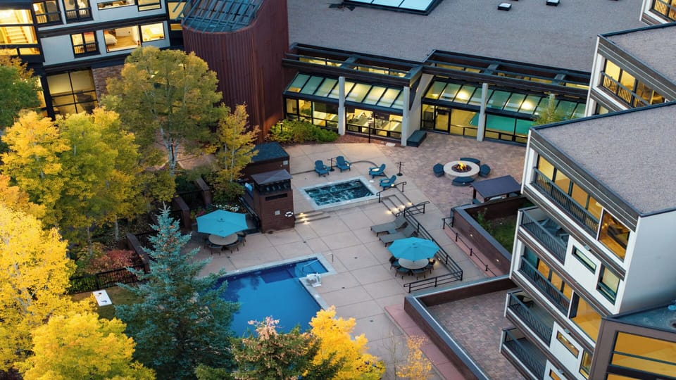 Aerial view of the property showcasing outdoor pool, hot tub, fire pit, and BBQ facilities surrounded by vibrant autumn foliage and modern multi-level buildings with private balconies.