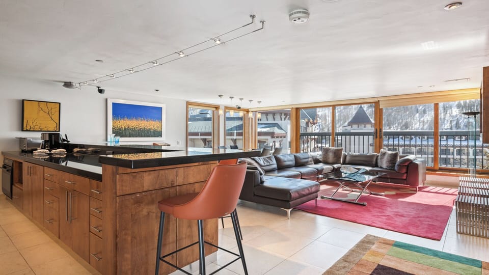 Sunlight floods through expansive windows framing snowy mountain vistas, while the open-plan kitchen and lounge invite you to gather, cook, and relax in stylish alpine comfort.