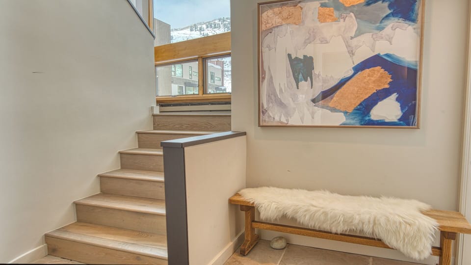 A cozy nook with a plush bench invites you to pause, while natural light pours in from mountain-view windows above the warm wooden staircase—your gateway to the rest of the home.