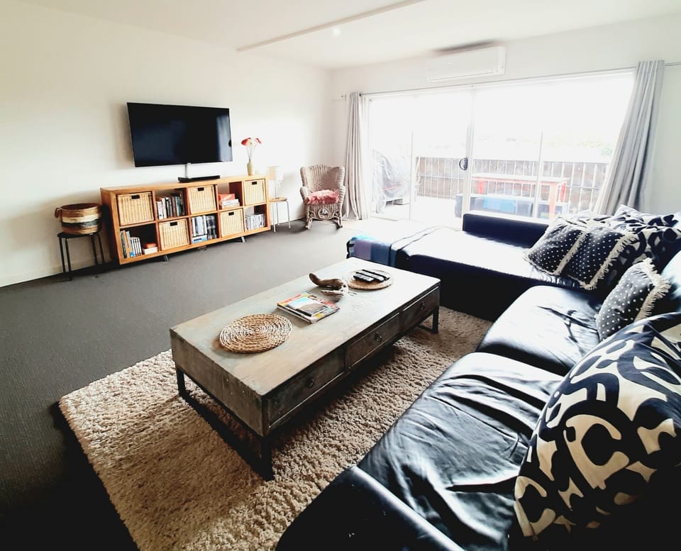 Lounge area with large black leather couch, smart tv, dvd, aircon, balcony.