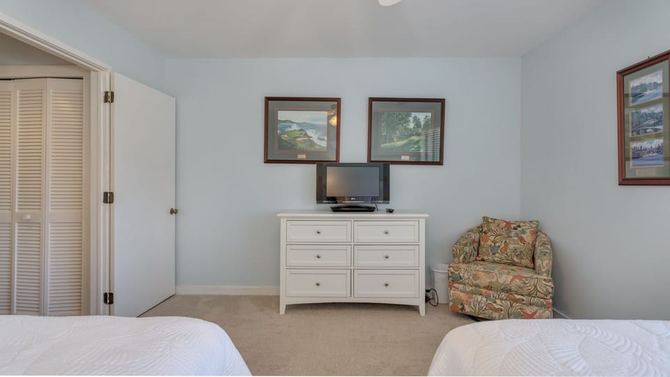 A flat-screen TV, generous dresser storage, and a comfortable reading chair create a relaxed, functional space.