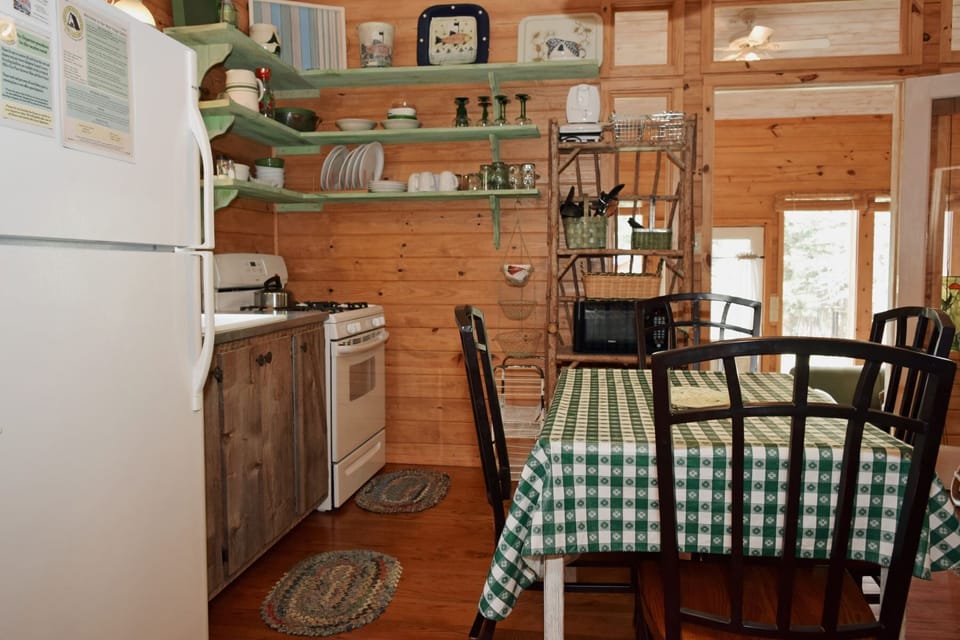 Your cozy cabin kitchen awaits with rustic wood walls, open shelving stocked with essentials, and a dining table ready for shared meals and morning coffee.