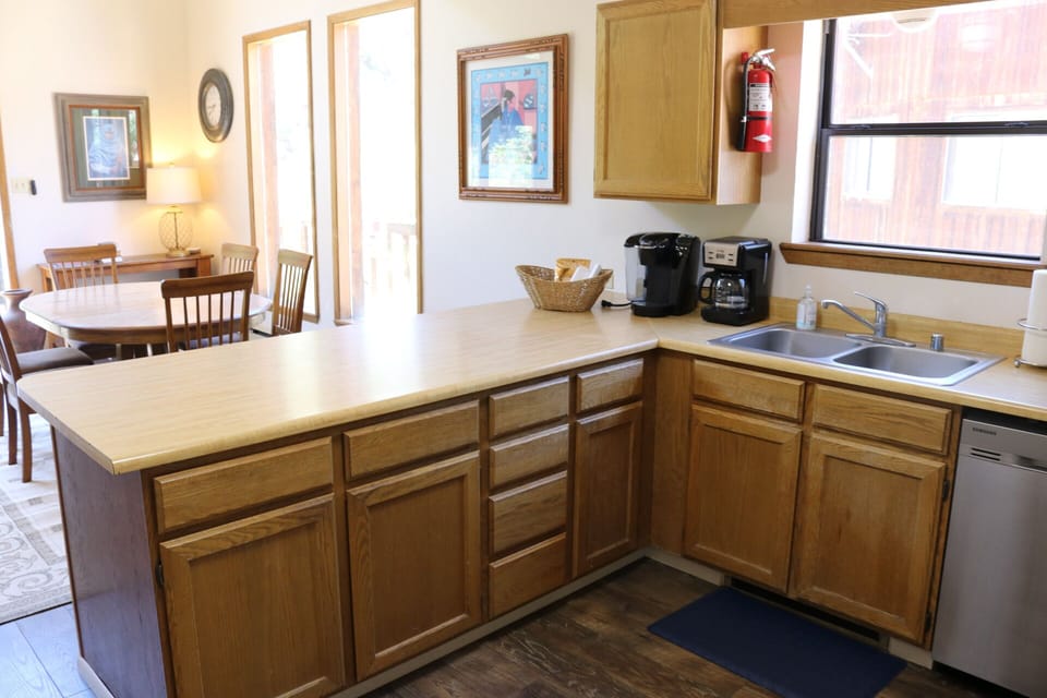 Your fully equipped kitchen with warm wood cabinets, double sink, dishwasher, and coffee makers makes meal prep easy while you enjoy natural light and charming artwork on the walls.