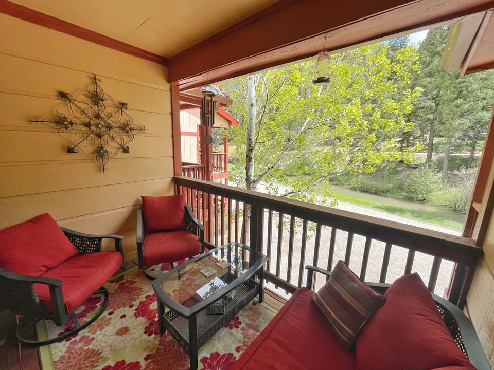 Relax on your private balcony with morning coffee, surrounded by lush trees and vibrant red seating that invites you to unwind and enjoy the peaceful scenery.