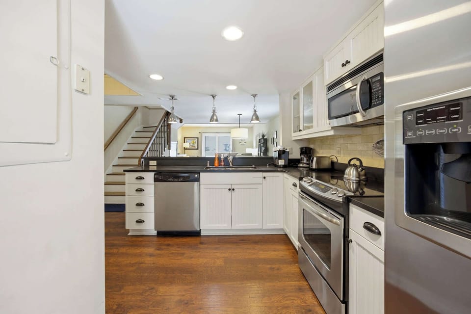 White beadboard cabinetry and deep counters anchor this airy chef's corner. Polished appliances gleam under recessed lighting, while the open layout flows past a breakfast bar into a bright, welcoming living space.