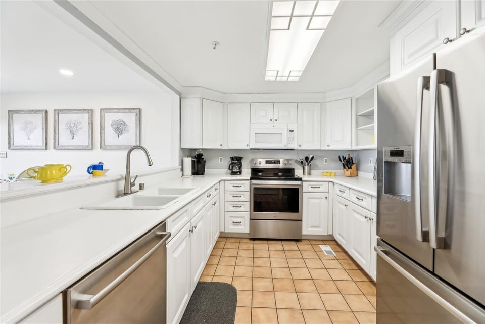 35 Kings Grant, Fenwick Island -Kitchen work space - Perspective of the kitchen showing the white double sink, stainless steel stove, and tiled flooring.