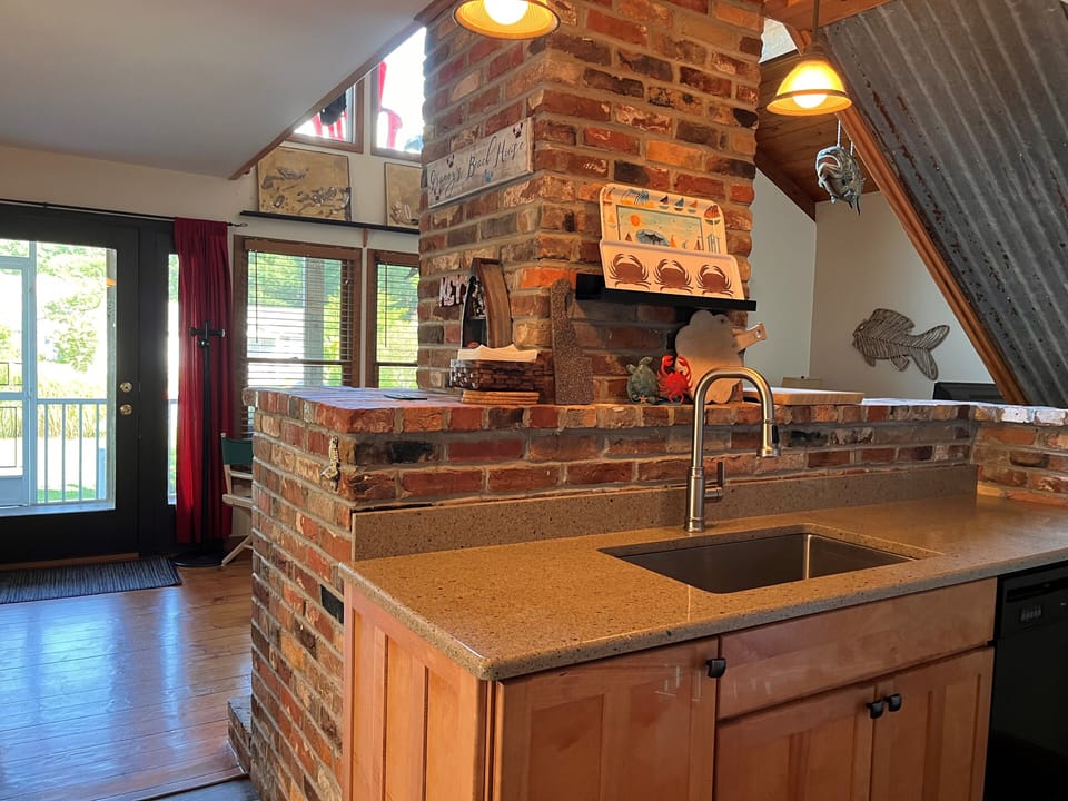 612 Paget Court - Unique Kitchen with Stone Accents - A view from behind the kitchen counter reveals the rustic stone pillar that houses the fireplace, creating a natural divide between the culinary and living spaces. The kitchen is well-equipped with modern appliances and ample workspace.