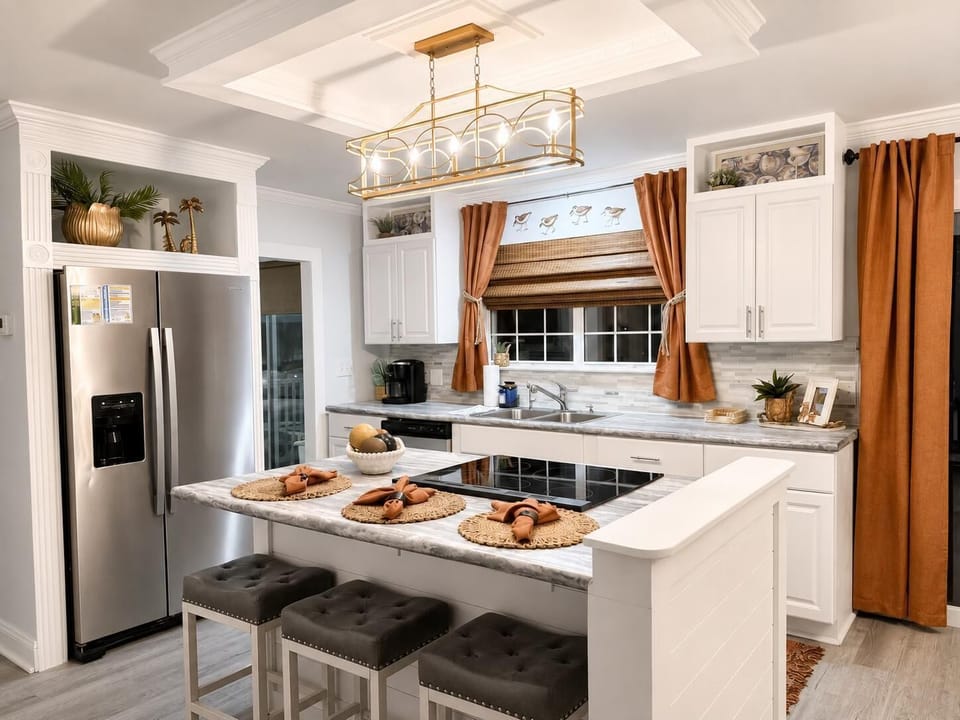 Marble countertops surround the cooktop island with tufted gray stools and copper-tone curtains in the kitchen.