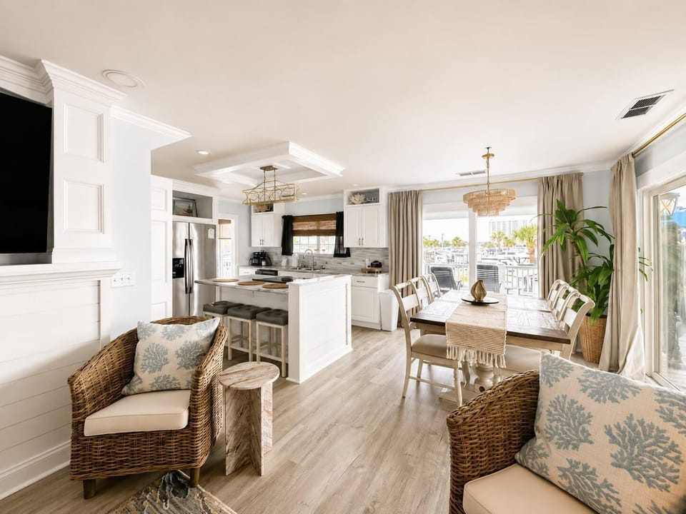 Open-plan kitchen and dining area with white cabinetry, wood floors, wicker chairs, and sliding glass doors.
