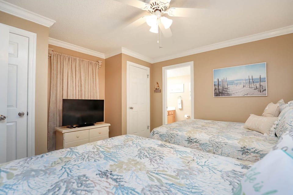 Two queen beds with colorful bedding and a TV create a relaxed atmosphere, complemented by beach artwork on the wall