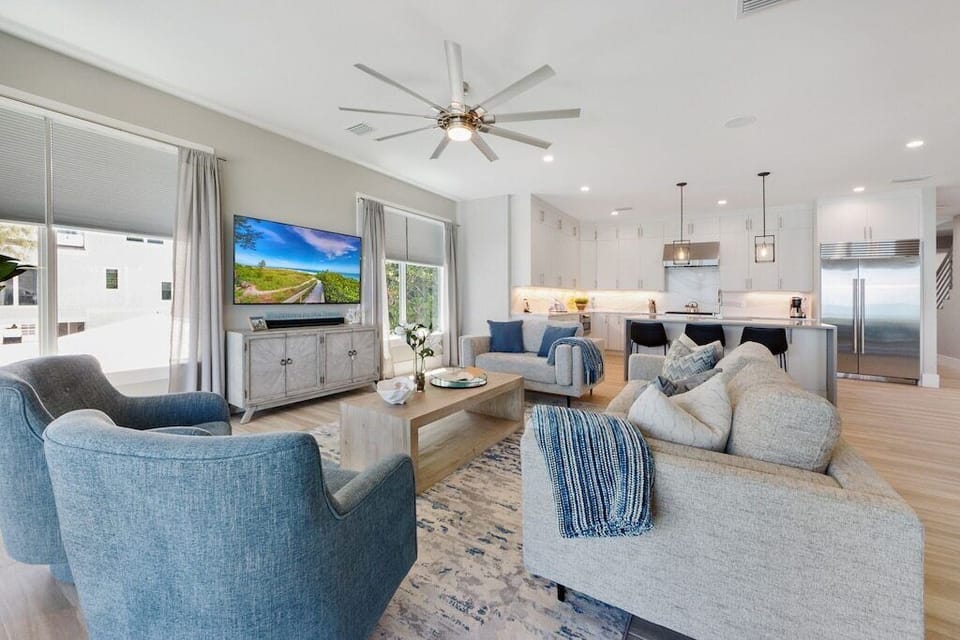 Immerse yourself in our chic living space, where comfort meets style. Sunlight bathes the room, highlighting the sleek kitchen and cozy furnishings. 