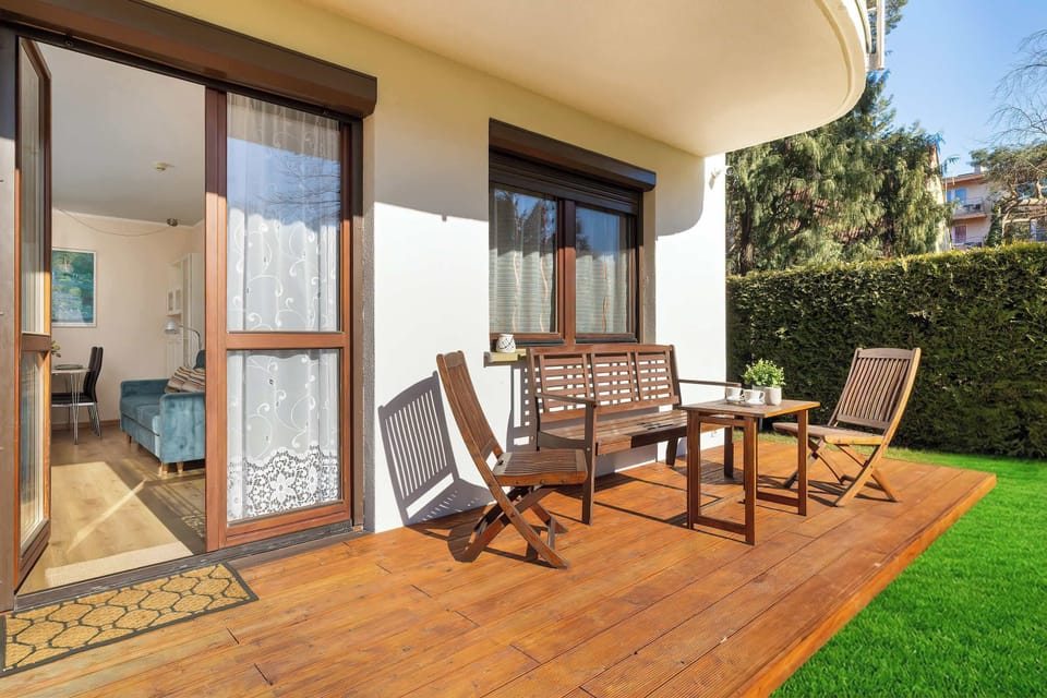 Another view of the patio and garden area shows outdoor seating placed near the building. The facade includes large windows and balconies above. The space looks ideal for relaxing outside.