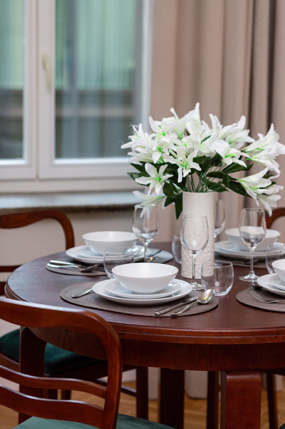 A dining table elegantly set with white flowers in a vase and polished glassware, adding a refined touch.