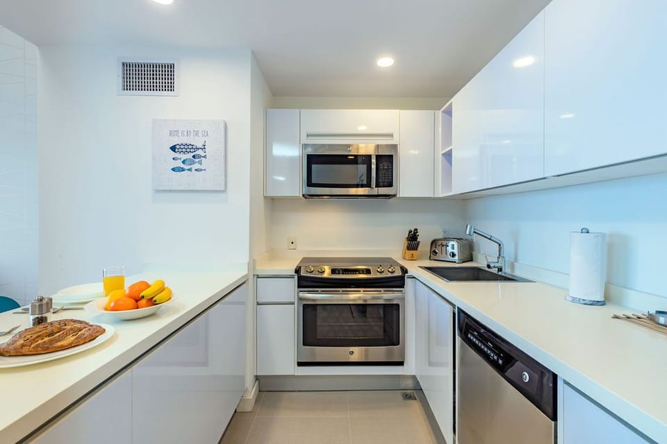 Your modern kitchen gleams with stainless appliances and sleek white cabinetry. Prepare meals on spacious counters, sip morning juice, and savor fresh fruit as sunlight fills this inviting culinary space.