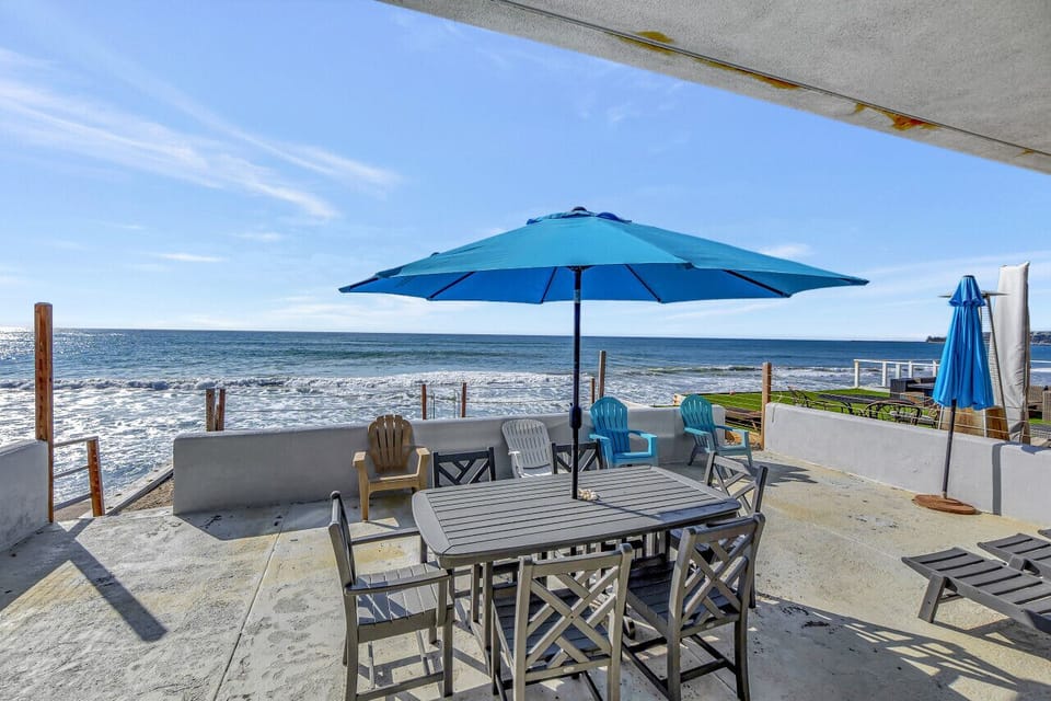 Oceanfront patio w/ umbrella dining table & lounge chairs overlooking the sparkling shoreline