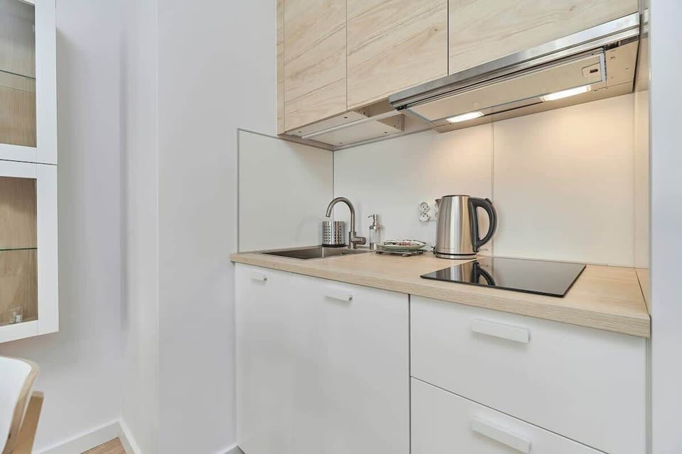  A compact but fully equipped kitchen with modern appliances. There’s a kettle, an induction cooktop, and clean, bright cabinetry.