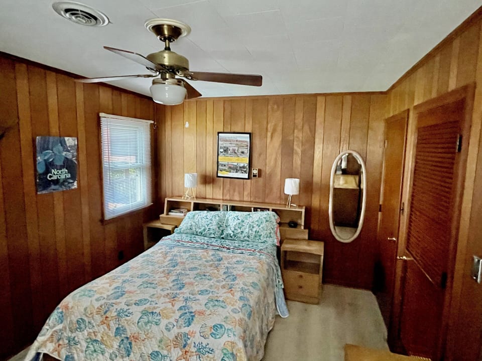 Relax in your cozy wood-paneled bedroom with tropical bedding, ceiling fan, and vintage charm that creates the perfect retreat.