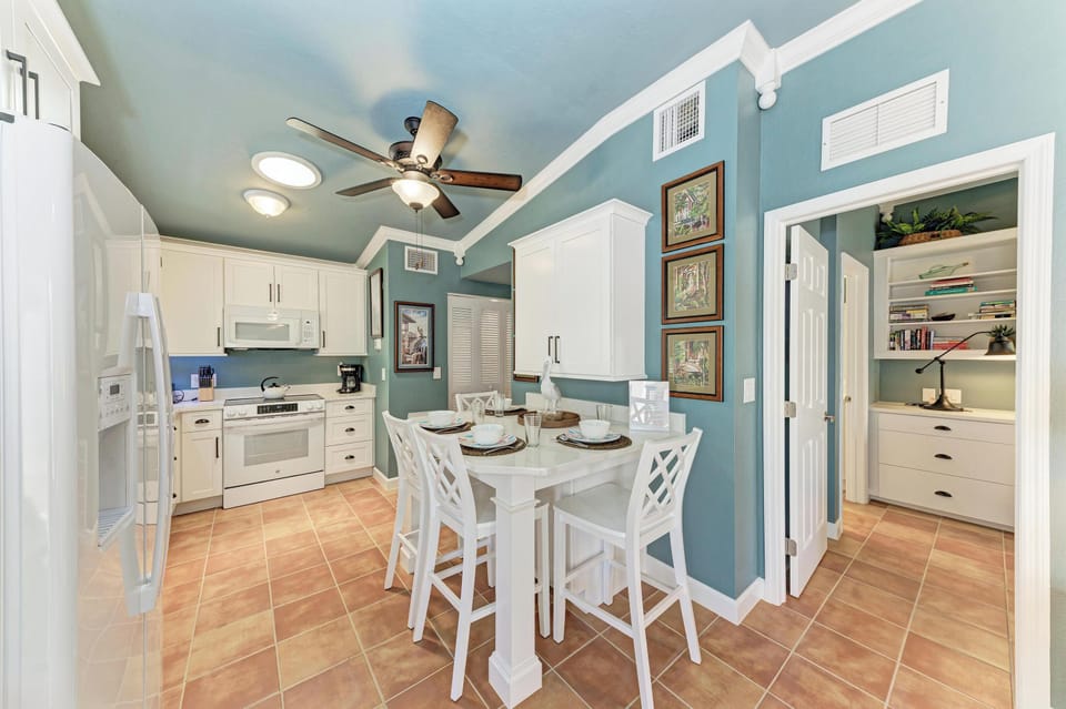 Step into your charming coastal-inspired kitchen and dining nook, where soft aqua walls and warm terracotta floors invite leisurely meals under the gentle hum of the ceiling fan.