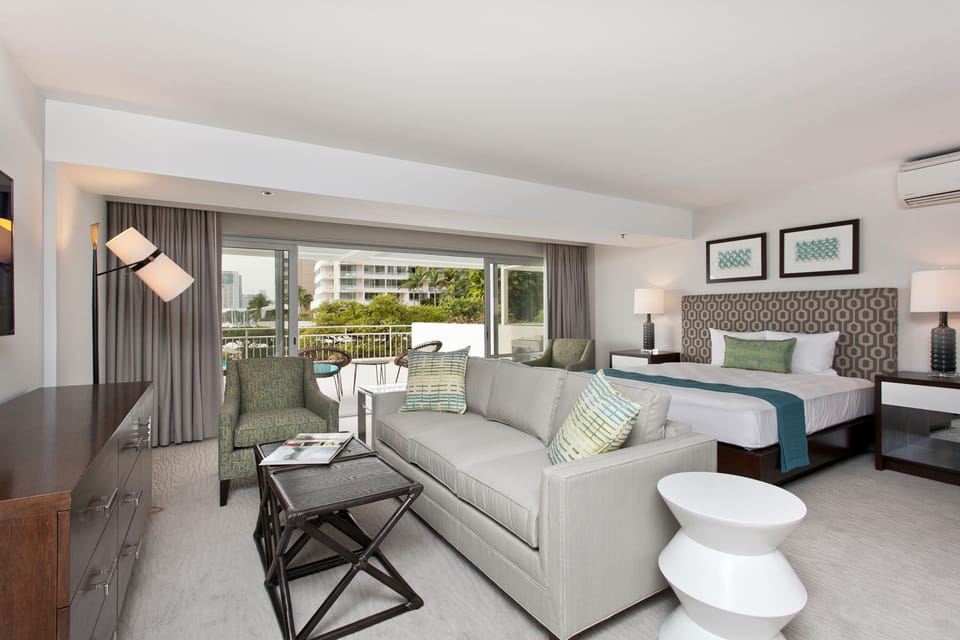 Step into your spacious suite with modern coastal flair, where a plush sofa invites you to unwind, a cozy king bed awaits restful nights, and your private balcony opens to refreshing outdoor moments.