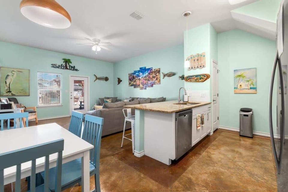 Open Floor Plan — Blue Dining Table, Kitchen Island, Gray Sectional, Reef Canvas & 'Treasure Island' Sign