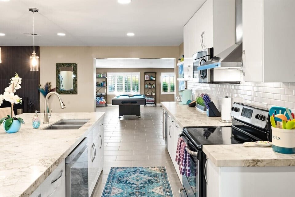 Open-concept chef’s kitchen featuring sleek countertops, modern appliances, and a direct line of sight to the pool table.