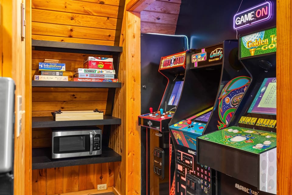 A dedicated game nook featuring classic arcade machines, board games, and a microwave snack station.