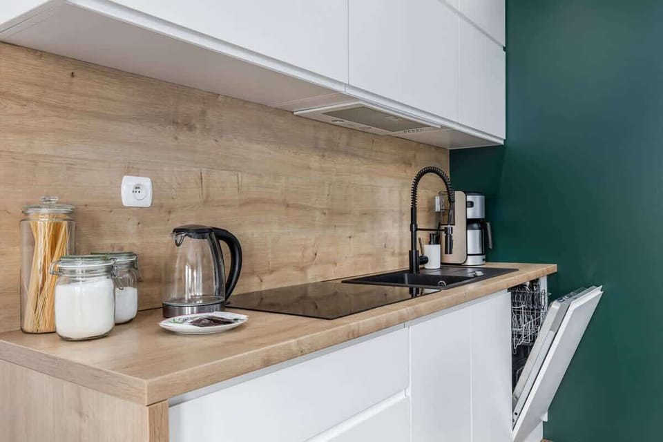 A close-up of a kitchenette featuring white cabinets, a compact design, and small appliances such as a kettle and coffee maker.